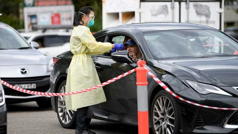 A woman in PPE gear tests someone at a drive-through testing clinic.