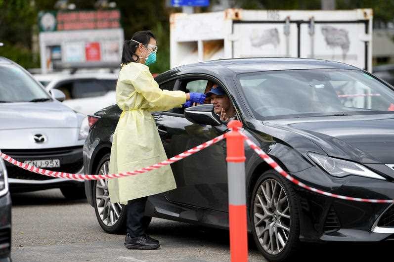 A woman in PPE gear tests someone at a drive-through testing clinic.