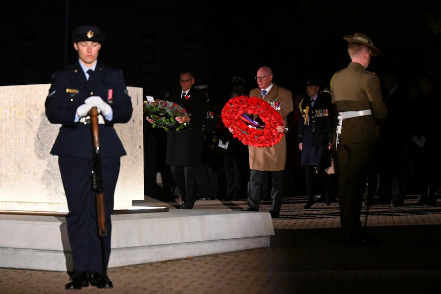 Men holding large wreathes prepare to put them down at a shrine at dawn.