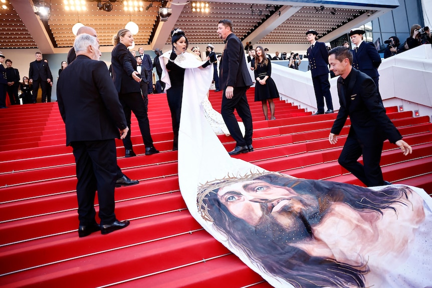 Massiel Taveras con vestido largo negro con guantes negros y capa larga blanca con el rostro de Jesús