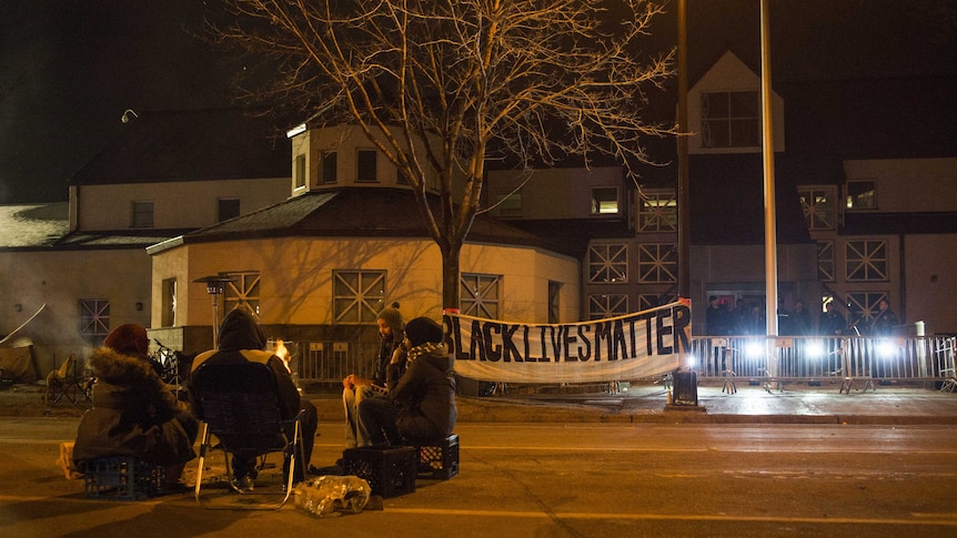 A group sits outside of the police station after five people weer shot.