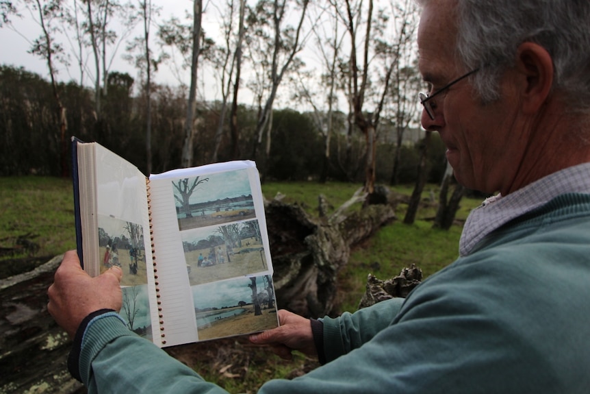 A man holding a photo album near a dried lake