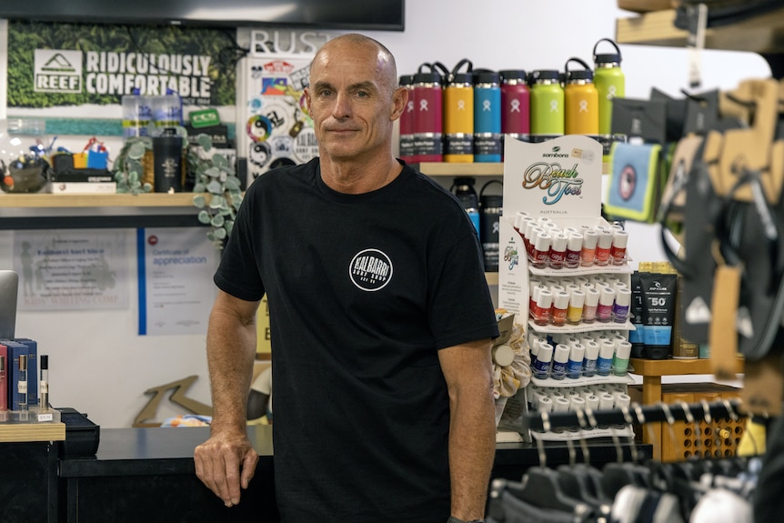 Bald man in black tshirt stands in surf shop