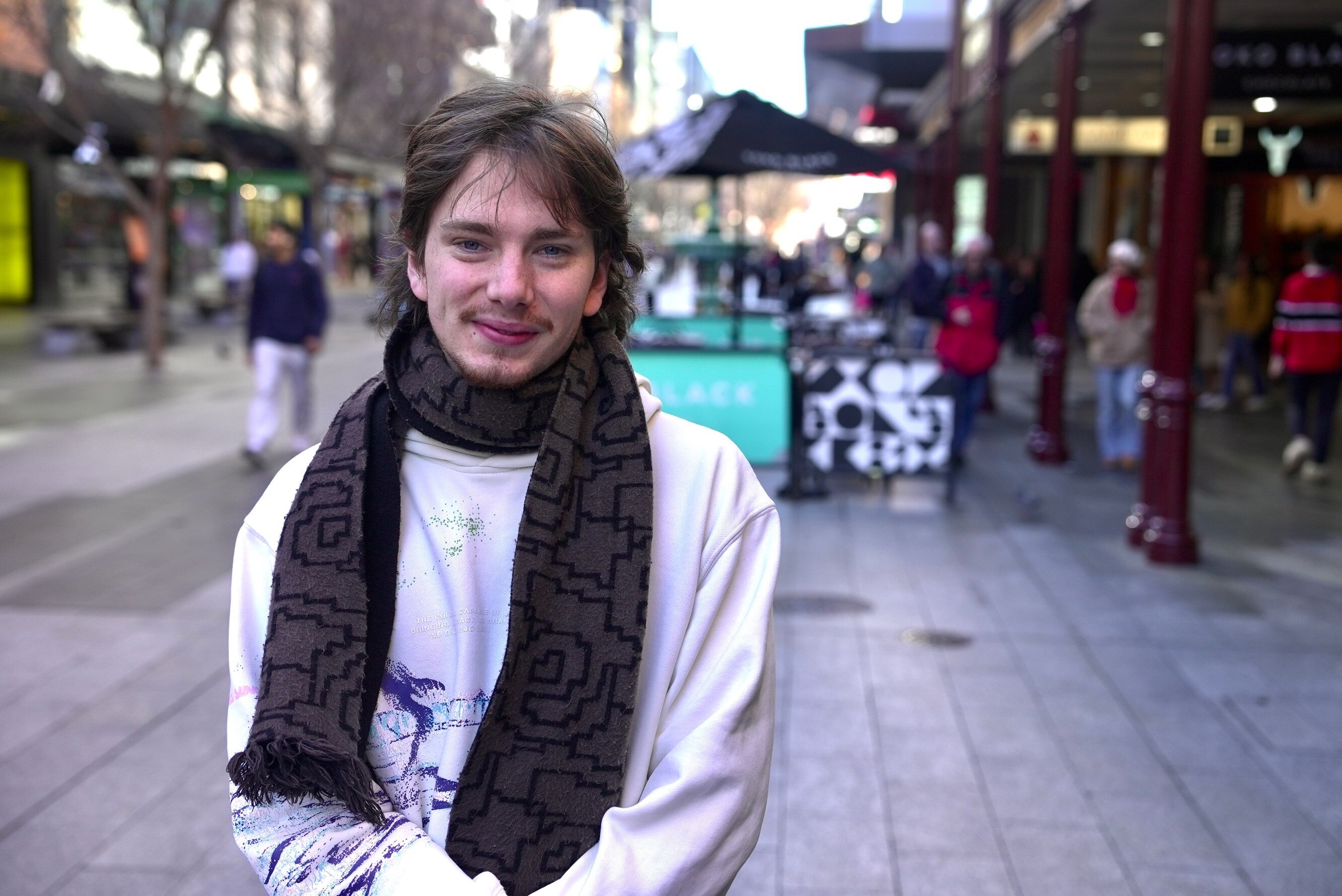 A young man with a scarf around his neck stands in a shopping mall.