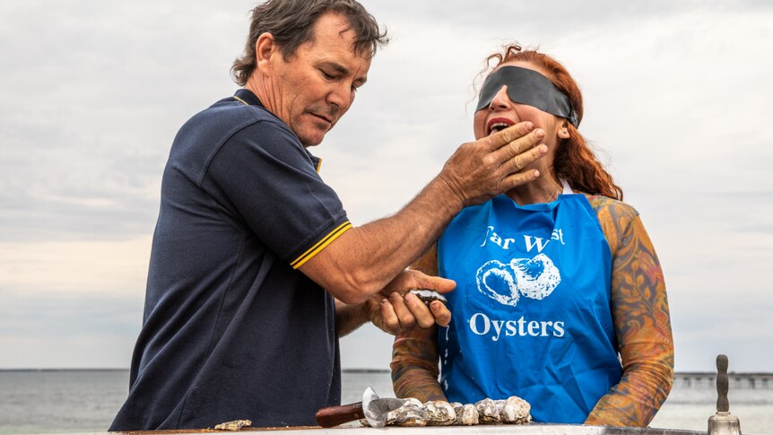 A man feeding a woman oysters while blindfolded. 
