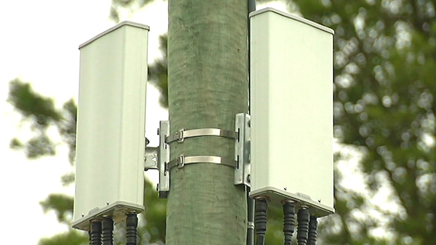 Two small cell boxes attached to a pole in Sydney. There are wires connected to the bottom of each box.