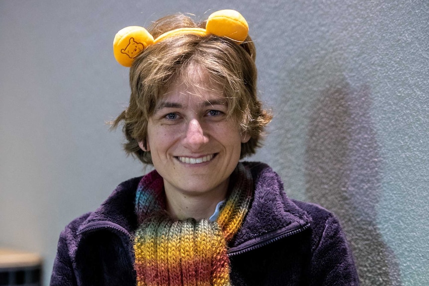 A woman holding Winnie the Pooh dolls and headband, smiling to camera.