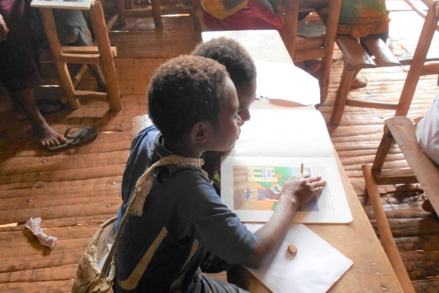 School kids sit around reading a picture book in a Papua New Guinea classroom