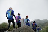 Five people walk on a trail on a foggy day.