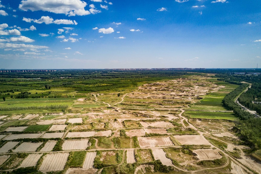 Yonging's dry, sandy riverbed rests among vibrant green fields contrasted with brilliantly blue skies with city in background.