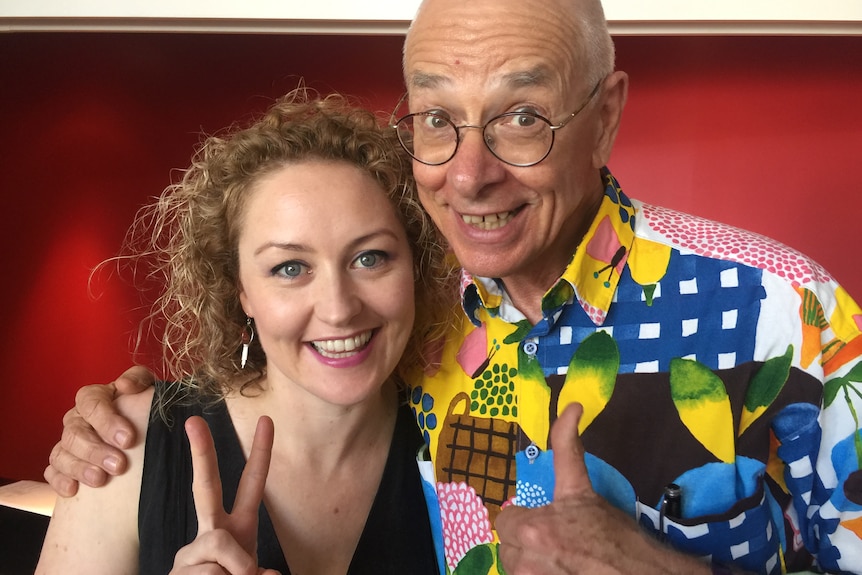 Man and woman with arms around each other. Woman does peace sign and man thumbs up sign.