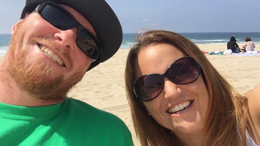 Sandy Casey and a man smile for a selfie on a beach.