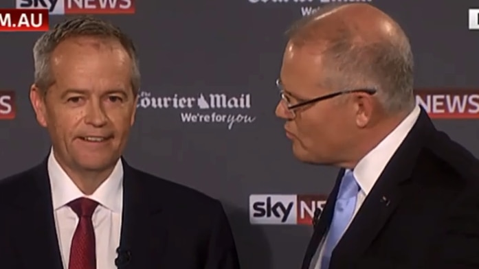 Scott Morrison, right, leans into Bill Shorten, left. They are wearing suits and are against a newspaper logo backdrop.