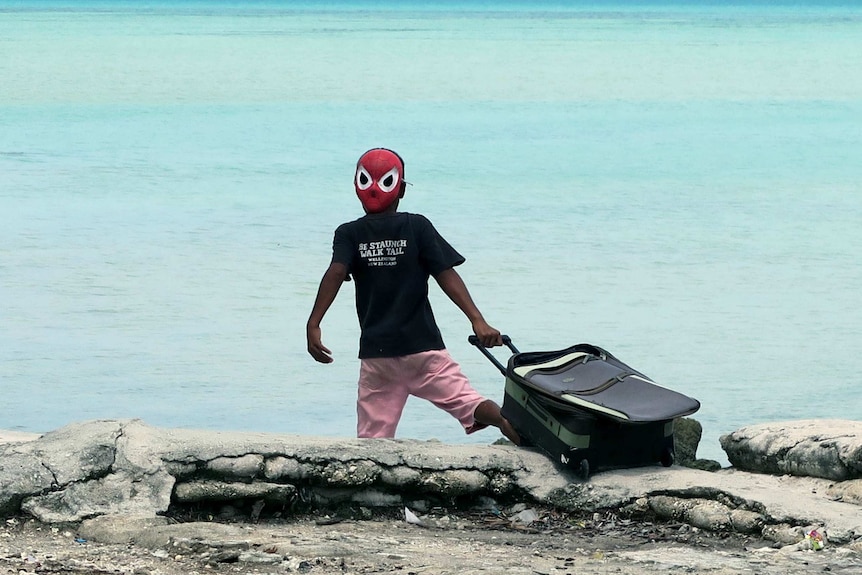 A boy in a spider-man mask drags a suitcase