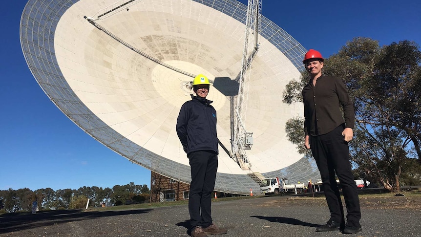 Two researchers stand in front of the CSIRO Telescope at Parkes.