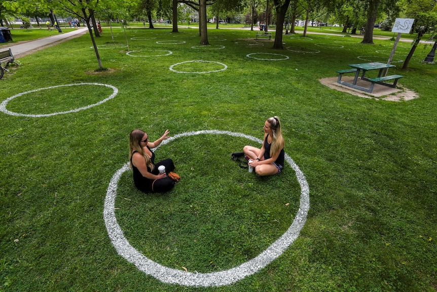Two women in a park sitting inside a white circle painted on the grass