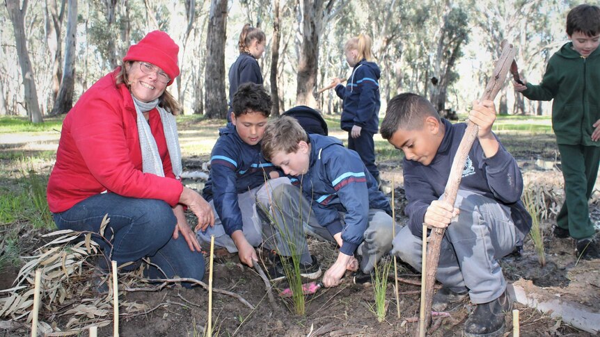 A smiling woman with a group of students planting seeds in bushland