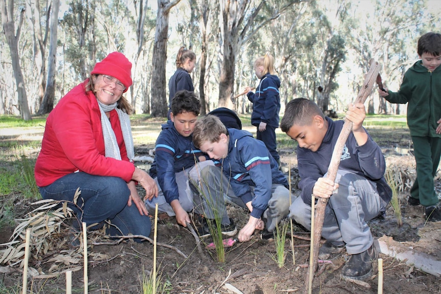 A smiling woman with a group of students planting seeds in bushland