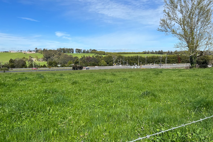 A green paddock is in the foreground with a road and intersection and more green rolling hills in the backg