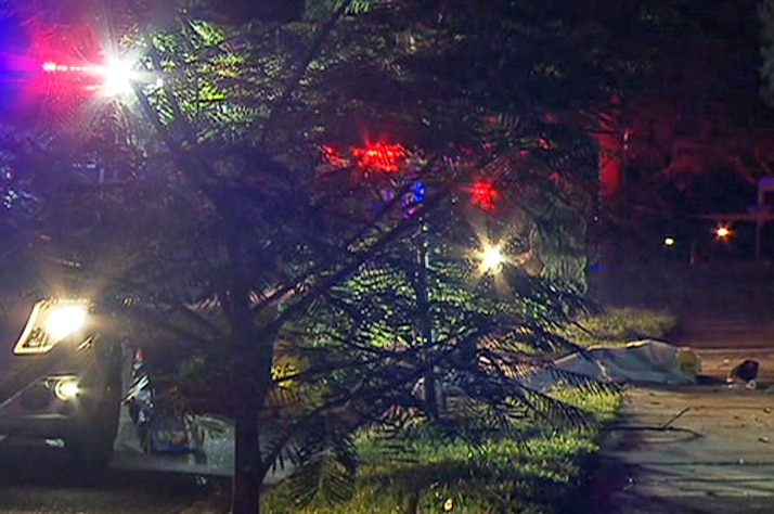 The body of a man who was stabbed to death lies under a sheet on the footpath of an Annerley street next to an ambulance.