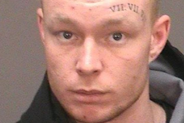 A man with a tattoo above his eyebrow stares at the camera.