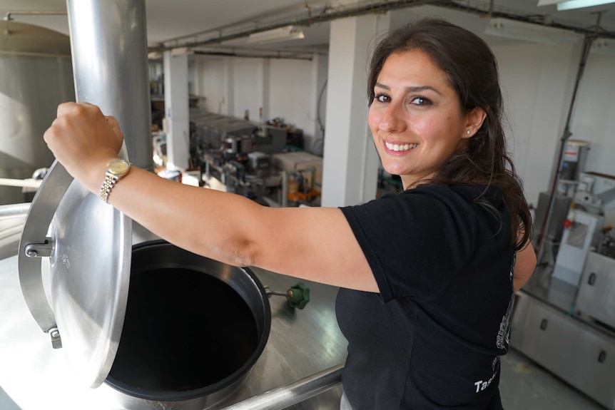 A smiling woman lifts the lid on a steel vat