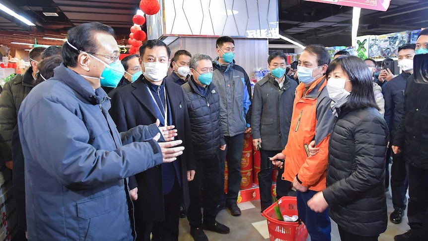 Chinese Premier Li Keqiang, wearing a blue face mask, holds his hands out as he talks to people in a shopping centre.