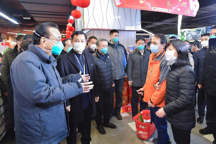 Chinese Premier Li Keqiang, wearing a blue face mask, holds his hands out as he talks to people in a shopping centre.