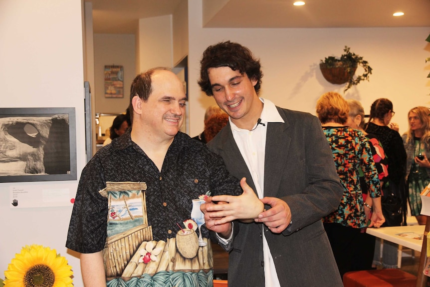 Two men smile in a crowded room. Ausnew Home Care, NDIS registered provider, My Aged Care