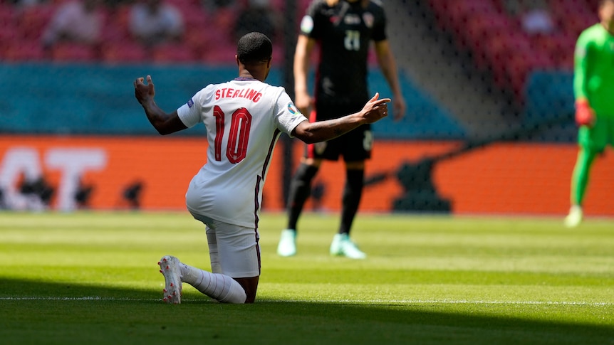 Raheem Sterling kneels with his arms outstretched