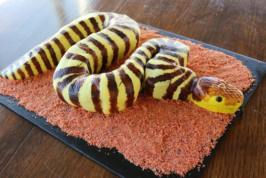 A cake in the shape of a snake, yellow with brown stripes.