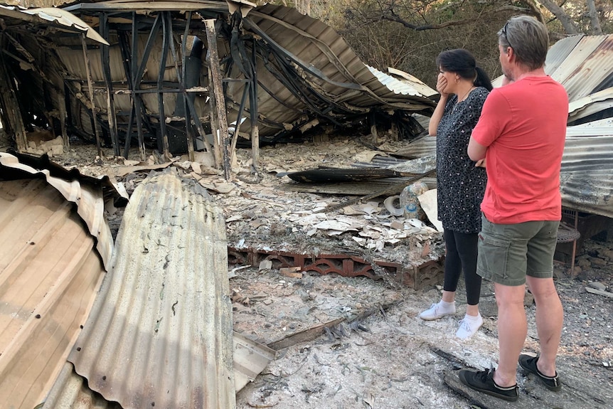 The Gordons stand among the charred debris of their bushfire-destroyed home at Cobraball.