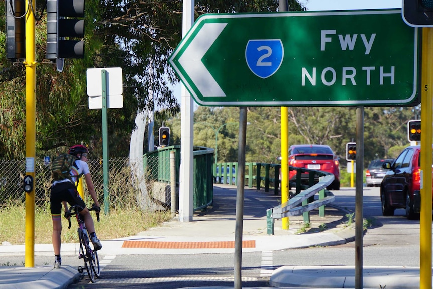 Cyclist waiting at traffic lights with Freeway North sign in foreground.