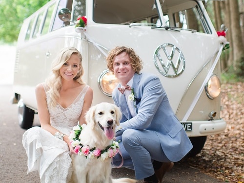 young bride and groom smiling in front of a combie van with dog.