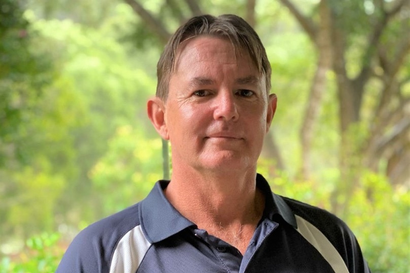 Man with blue top on standing against the the background