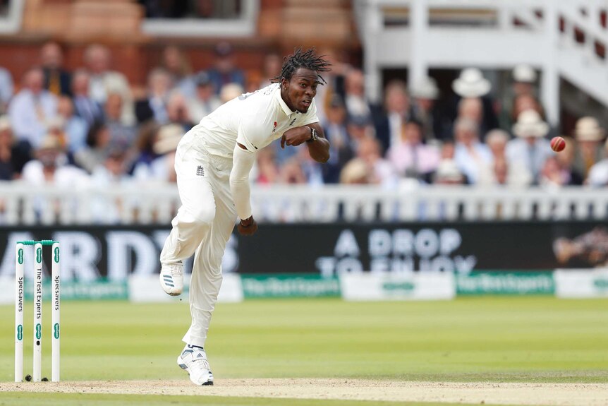 Jofra Archer delivers a cricket ball in his delivery stride with the pavilion at Lord's in the background.