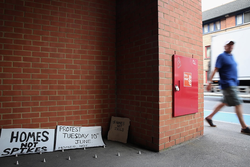 Metal spikes outside a private block of residential flats in London, with a sign saying 'homes not spikes' in the background.