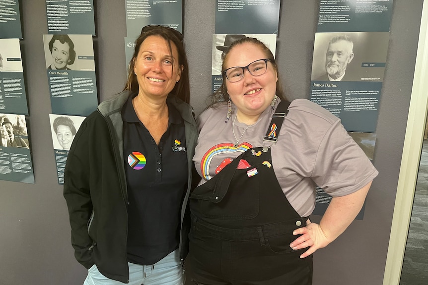 Two people wearing rainbow badges stand smiling.