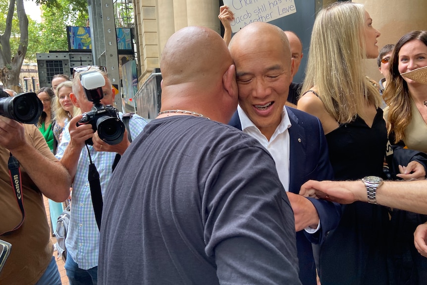 Bald man hugs another man in a crowd