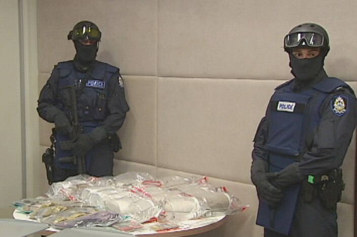 A stash of methylamphetamine and cash lies on a table at police HQ, guarded by two police officers