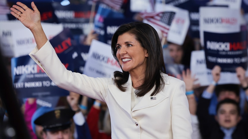 nikki haley standing and waving at presidential campaign with signs in background