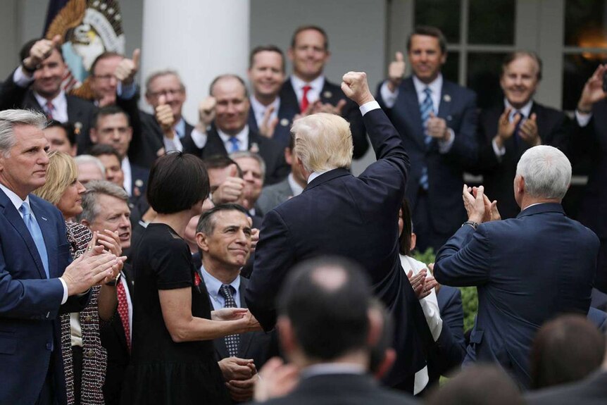 Trump has his back to the camera as he raises his fist victoriously towards Republicans