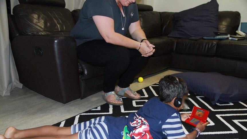 Unidentified foster mother watches her child play on an electronic game.