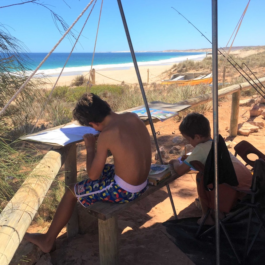 Brodie and Will Pittman do their school work outside their camper trailer on a beach at Red Bluff, Quobba Station, WA
