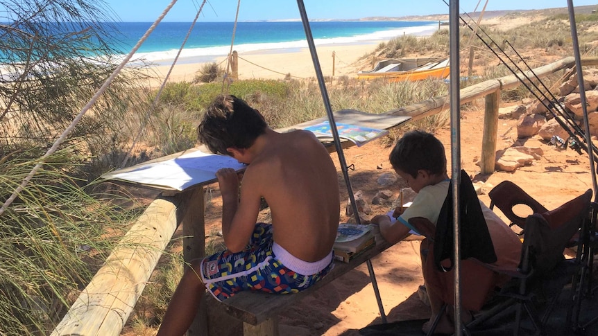 Brodie and Will Pittman do their school work outside their camper trailer on a beach at Red Bluff, Quobba Station, WA