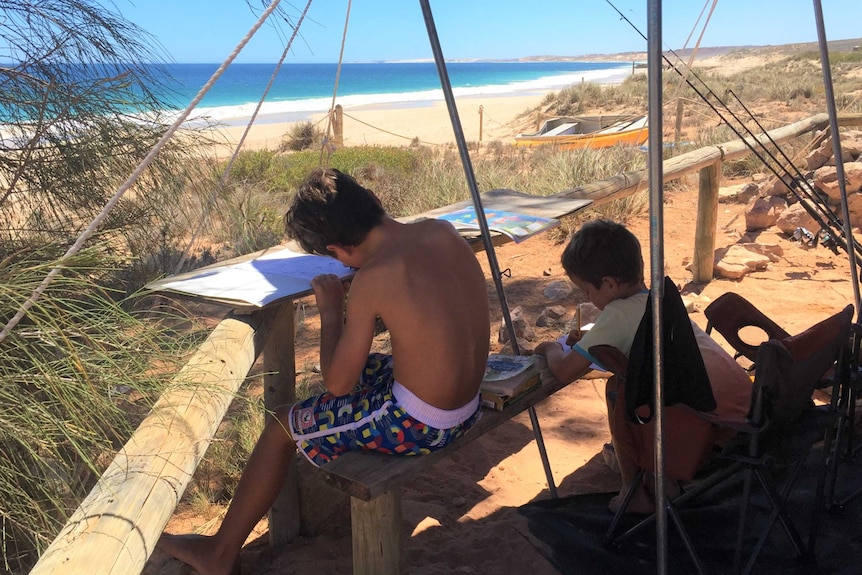 Brodie and Will Pittman do their school work outside their camper trailer on a beach at Red Bluff, Quobba Station, WA