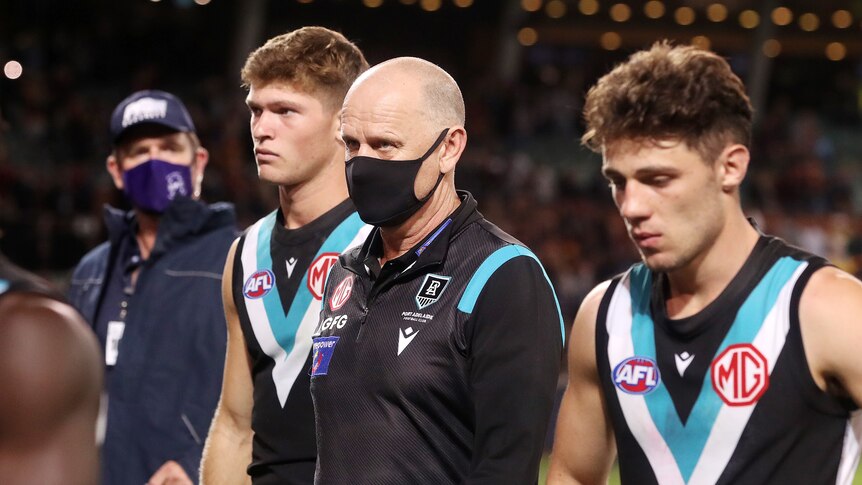 A mask-wearing AFl coach and his dejected players walk off Adelaide Oval after losing a game 