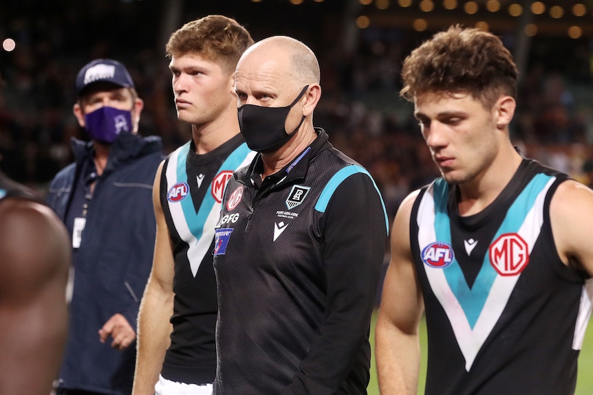 A mask-wearing AFl coach and his dejected players walk off Adelaide Oval after losing a game 