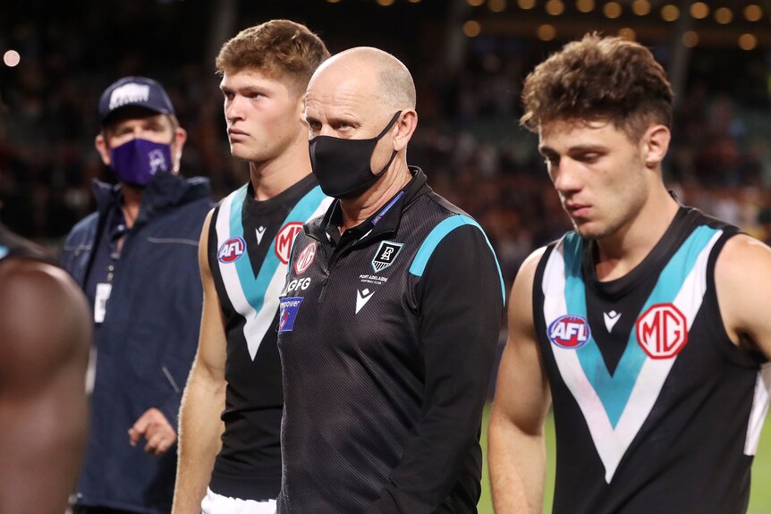 A mask-wearing AFl coach and his dejected players walk off Adelaide Oval after losing a game 