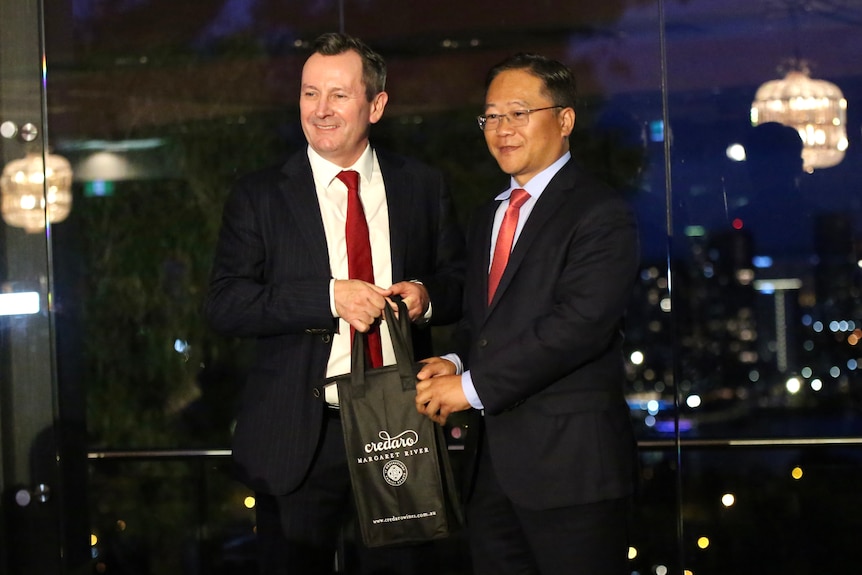 Mark McGowan smiles as another man in a suit hands him a two-bottle gift bag of wine